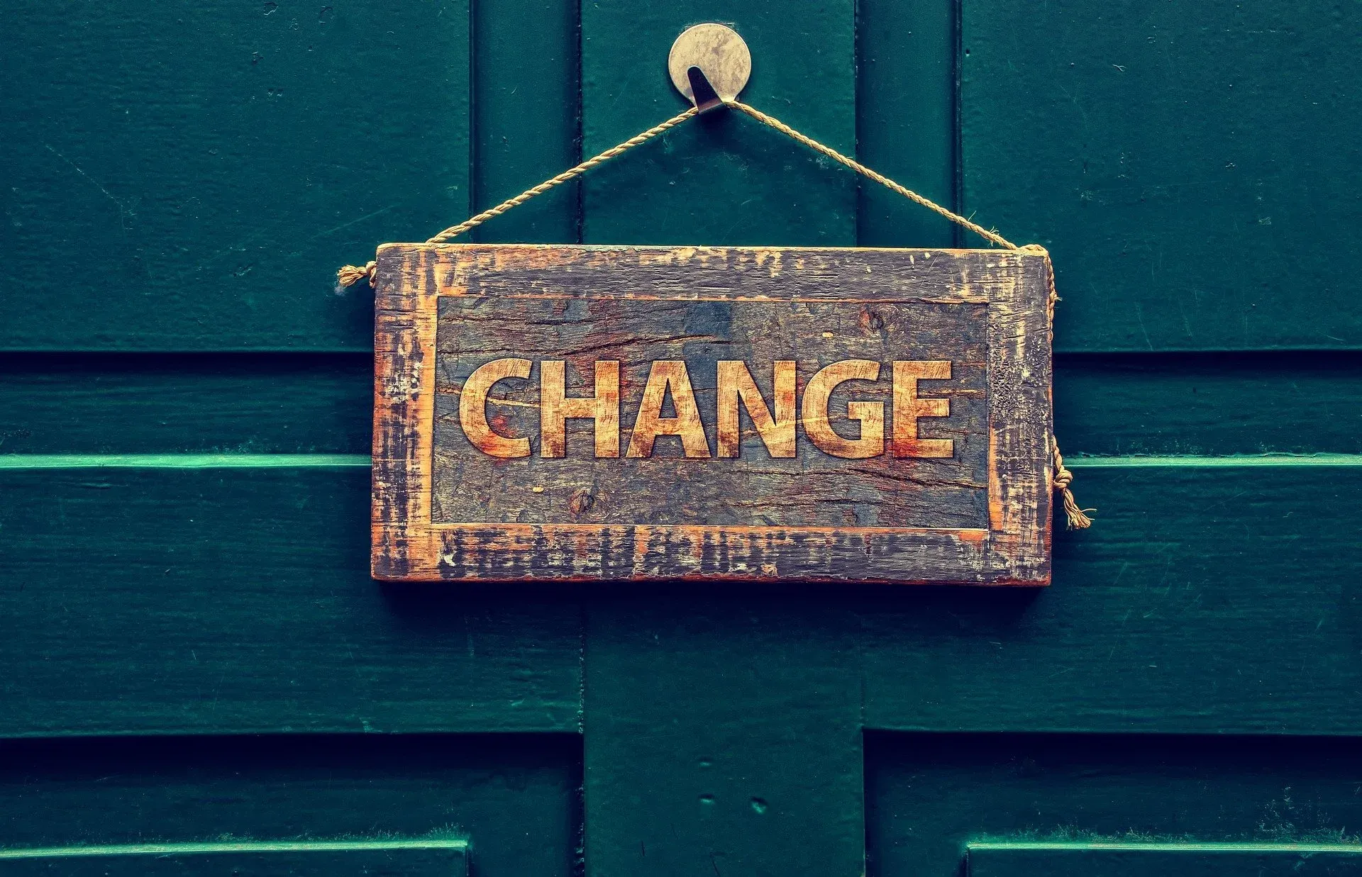A weathered wooden sign reading "Change" hanging by twine on a green painted door.